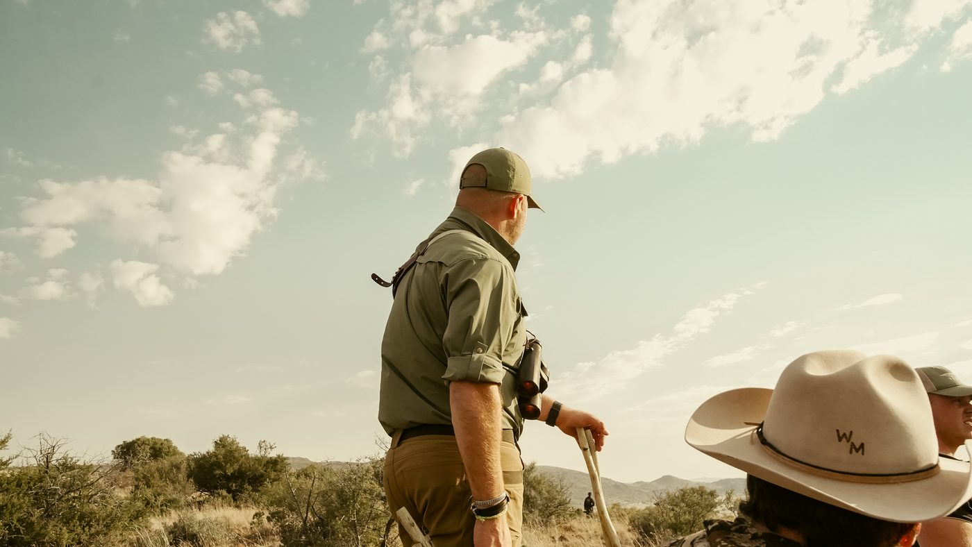 A guide walking a ridge with a rifle beneath a wide sky