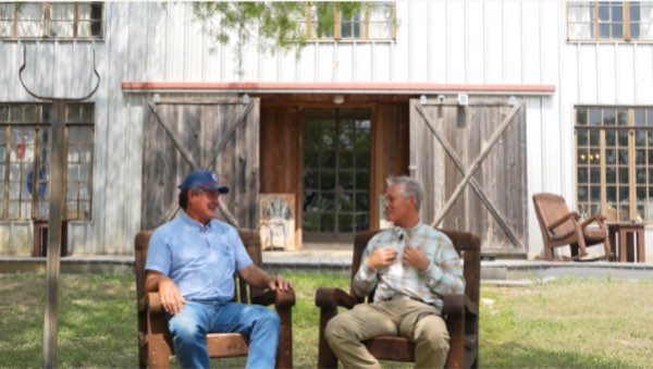 Two men in conversation in rocking chairs outside a ranch barn