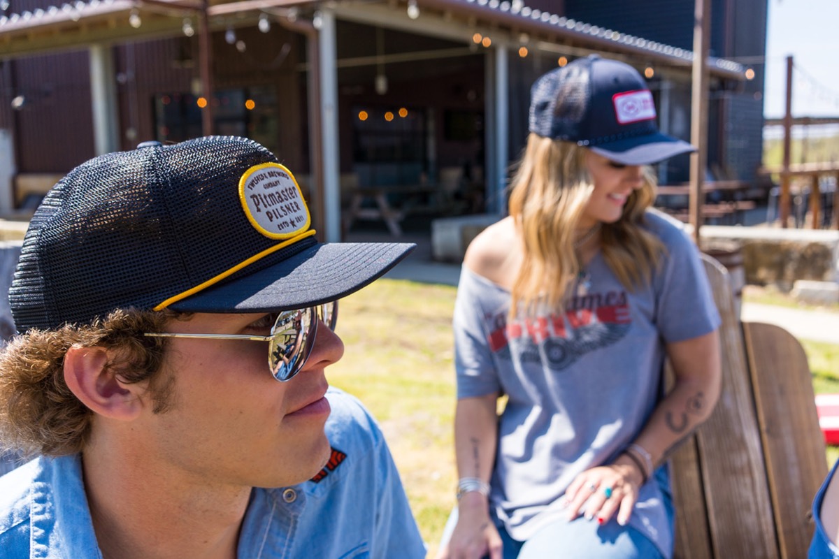 Two people in branded caps sitting outside a ranch barn