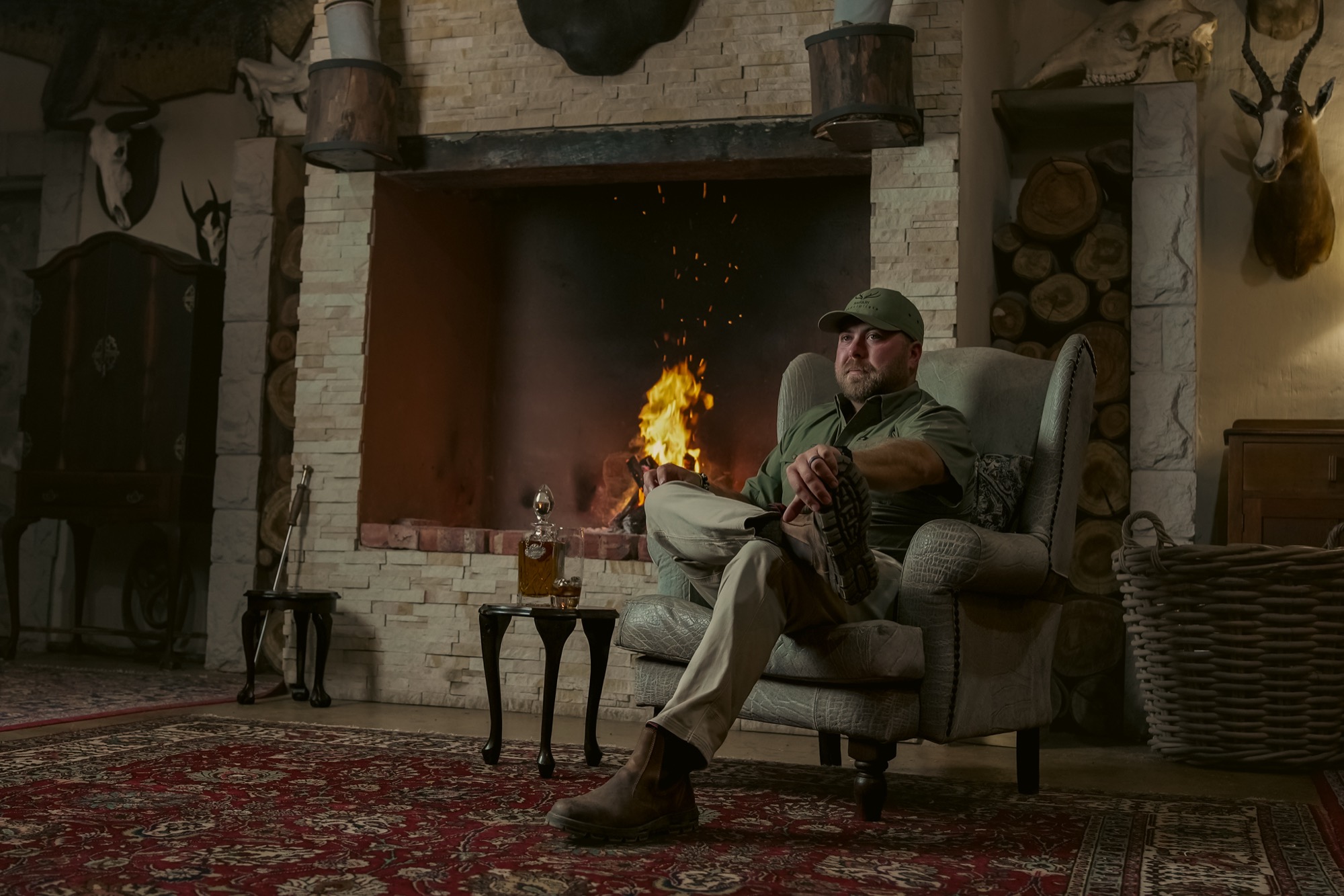 A guest seated in an armchair beside a lit fireplace in a hunting lodge