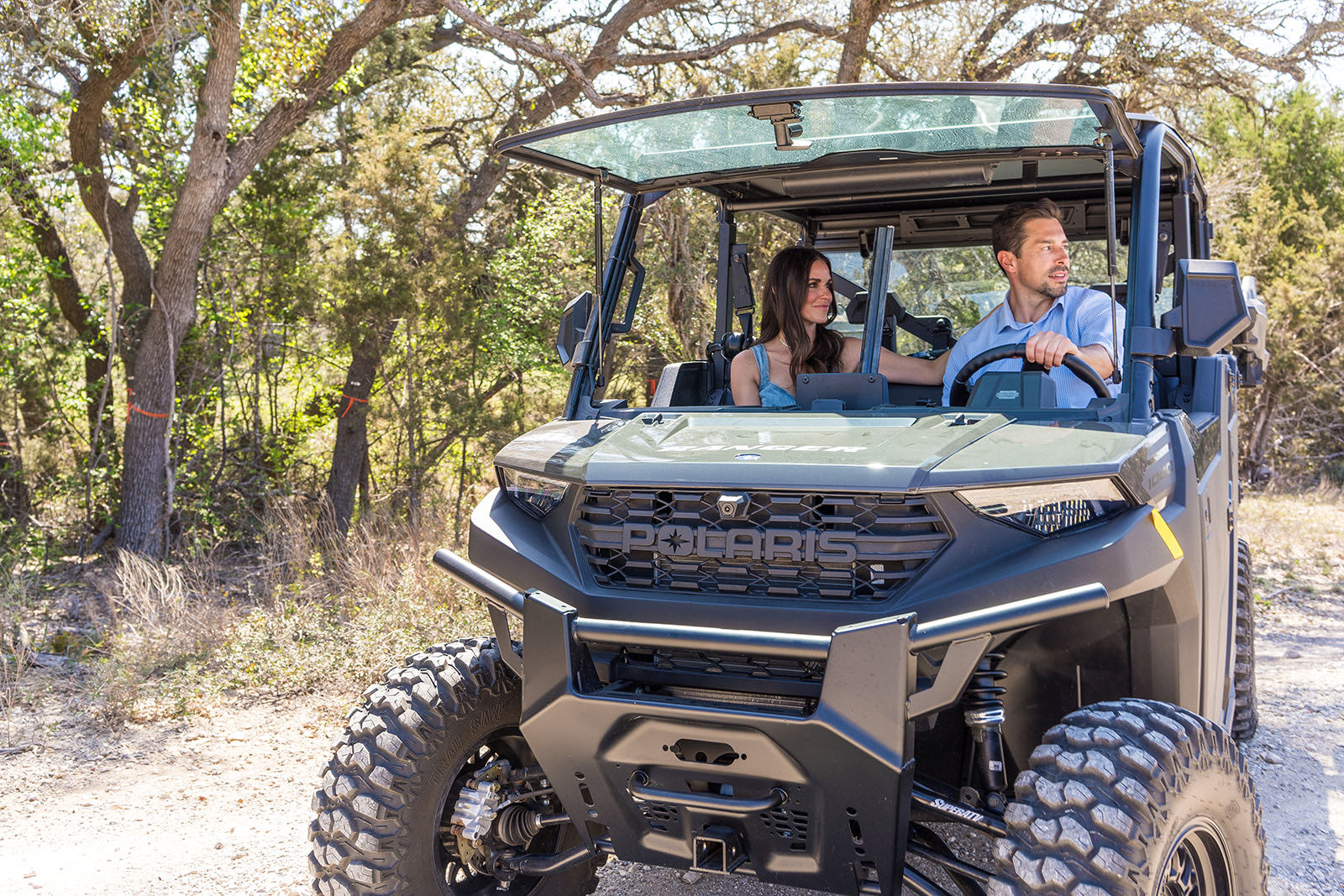 A couple driving a side-by-side along a ranch road beneath live oaks