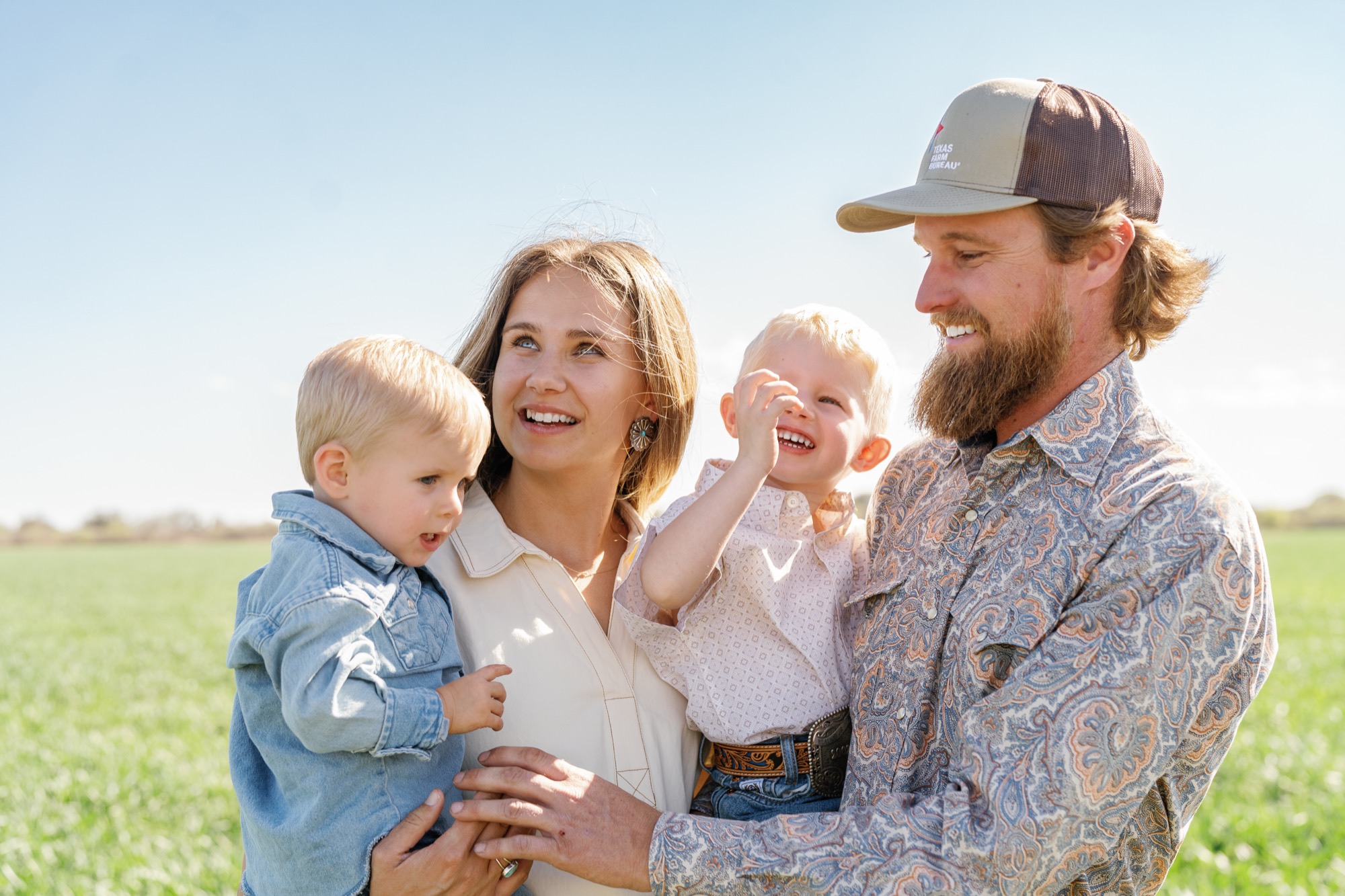 A family with two young children standing together in a green field